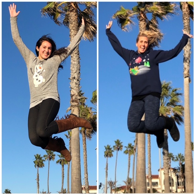 A brunette woman on the left, Jay, is jumping in the air and smiling. A blonde on the right, Shell, does the same.