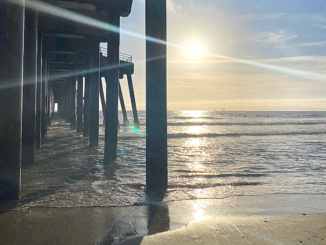 Sun rays cut from left to right across a photo of a beach pier.