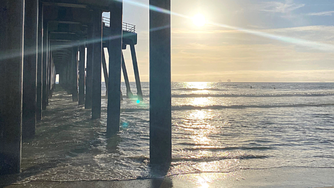 Sun rays cut from left to right across a photo of a beach pier.