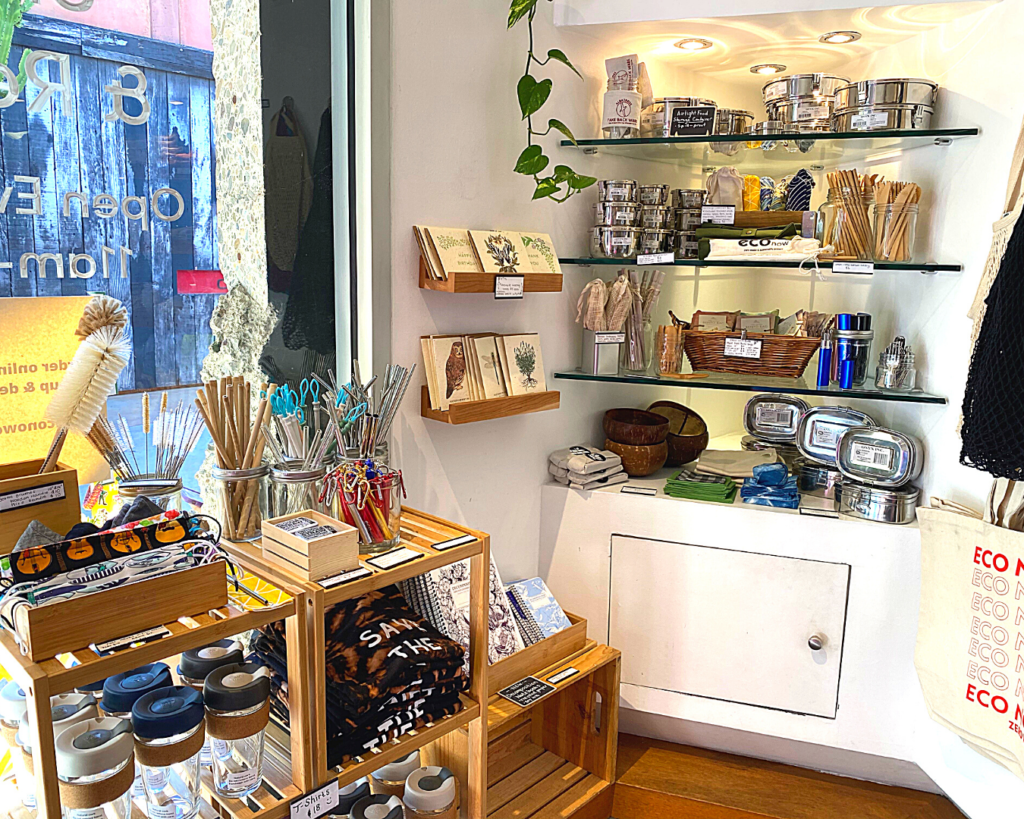 An array of shelves display a variety of eco friendly and zero waste products. These include reusable bags, bamboo toothbrushes, water bottles, Tupperware, post cards, journals and more! 