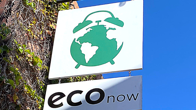 An outdoor sign for Eco Now, a zero waste shop in Costa Mesa, California. The logo features a blue-green earth as an alarm clock over a white background.